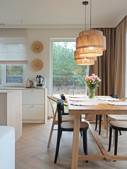 Jadalnia z drewnianym stołem, krzesłami z plecionką i lampami boho