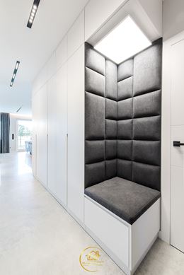 Białe szafy z szarym, narożnym siedziskiem w korytarzu