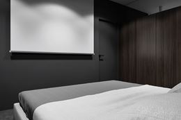 Czarna sypialnia z brązową szafą i ekranem projektora w suficie