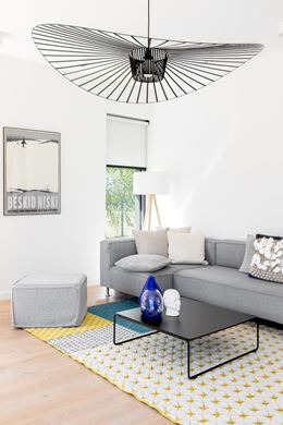 Biały salon z szarą kanapą i patchworkowym dywanem