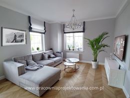 Prosto urządzony salon w stylu glamour z szarą kanapą