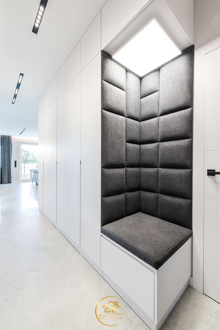 Białe szafy z szarym, narożnym siedziskiem w korytarzu