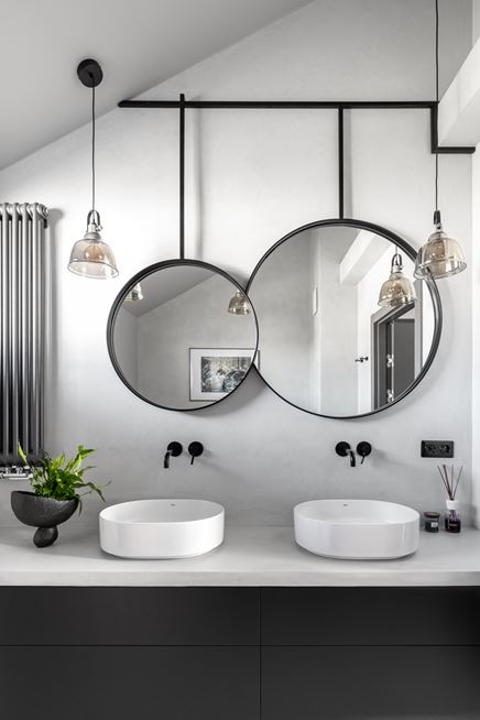 Asymetryczne lustro w czarnej ramie i industrialne oprawy oświetleniowe w łazience