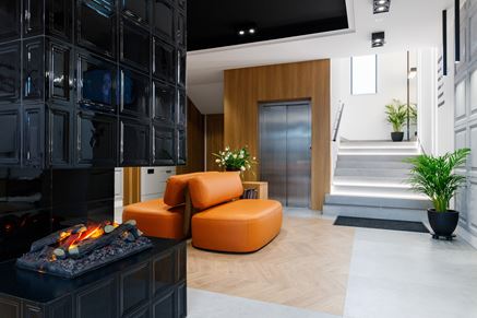 Poczekalnia z czarnym kominkiem i pomarańczowymi sofami