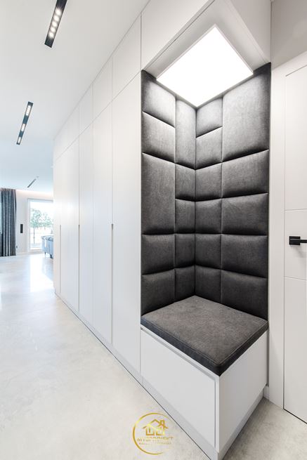 Białe szafy z szarym, narożnym siedziskiem w korytarzu