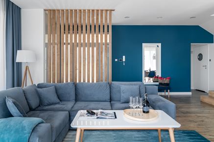 Salon z niebieską kanapą i ścianką z drewnianych kantówek