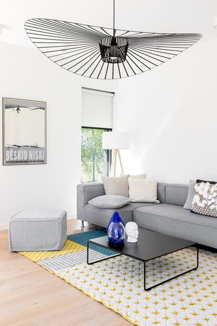 Biały salon z szarą kanapą i patchworkowym dywanem
