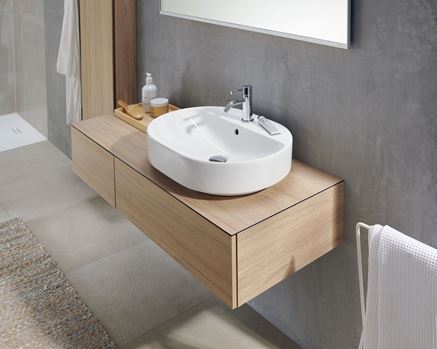 Szara łazienka z brązową szafką i białą umywalką z serii Geberit VariForm