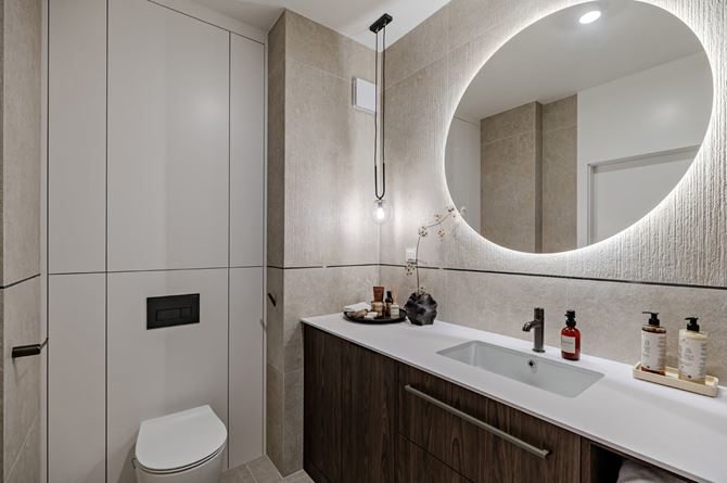 Jasna łazienka z okągłym lustrem i zabudową.jpg