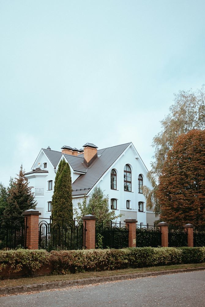 Biały dom z ogrodzeniem z czerwonego klinkieru i ażurowych, metalowych przęseł