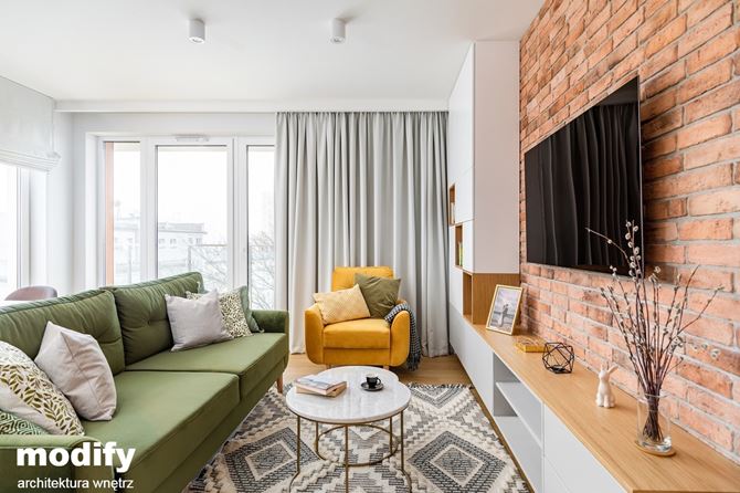 Biały salon z czerwoną cegiełką i zieloną kanapą