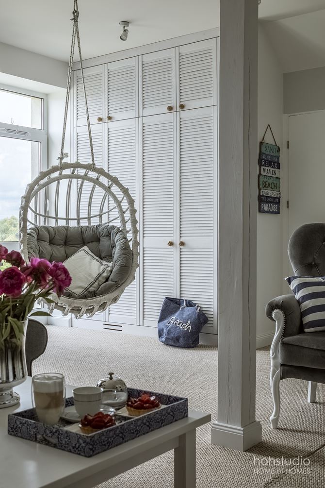Biała szafa z ażurowymi drzwiamii i wiszący fotel w salonie