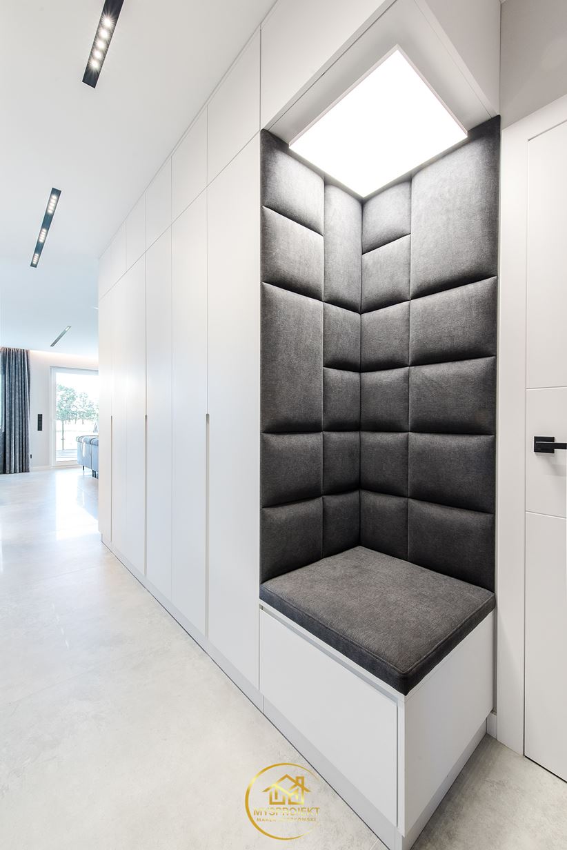 Białe szafy z szarym, narożnym siedziskiem w korytarzu