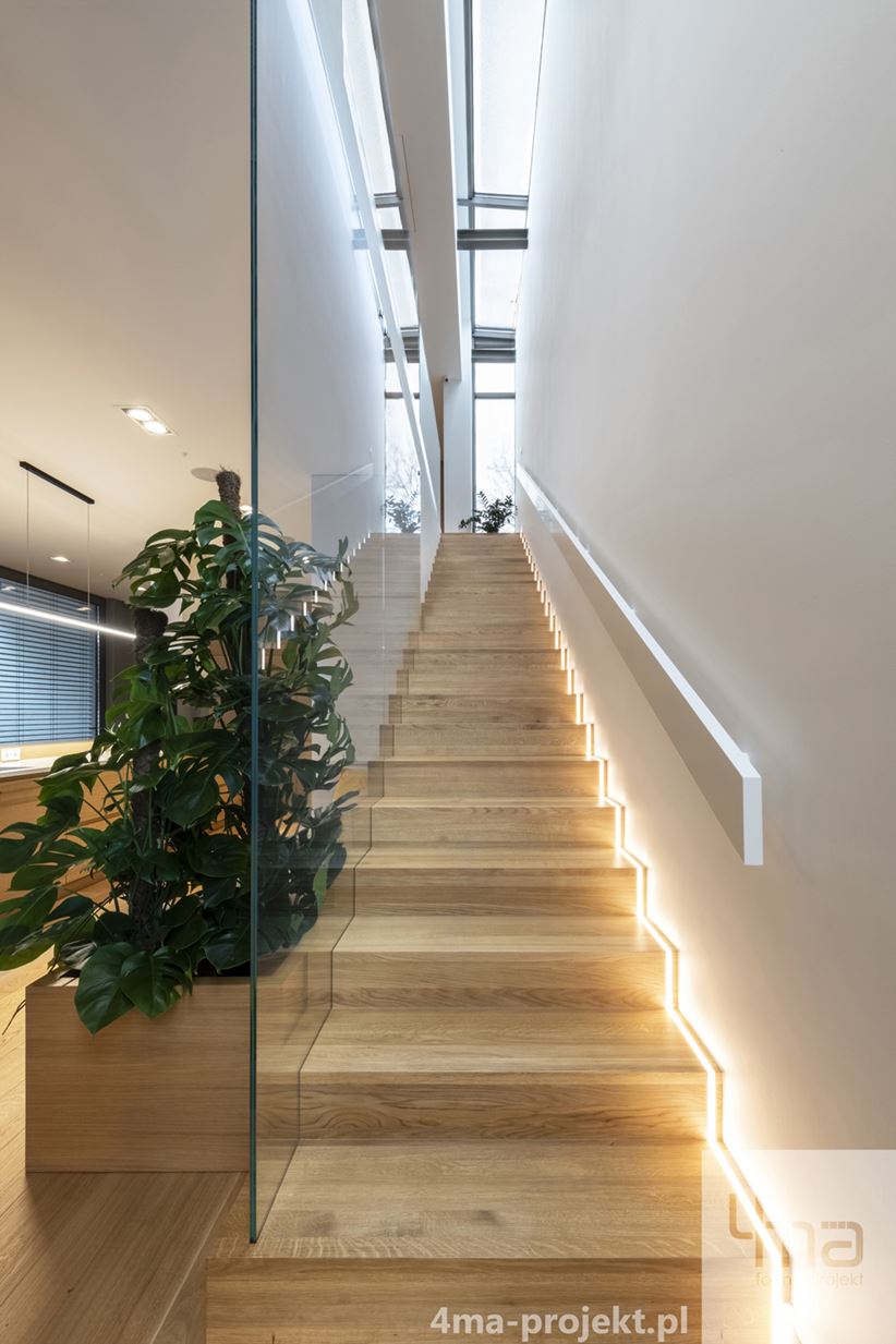 Drewniane schody podświetlane z wysokim przeszkleniem zamiast balustrady